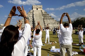 People raise their arms towards the sun while standing in front of the Kukulcan pyramid in Chichen Itza